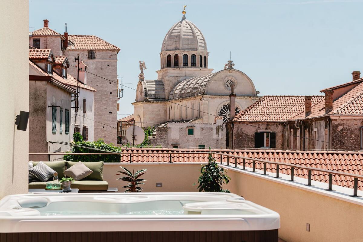 Une terrasse sur le toit avec un jacuzzi, une vue sur des bâtiments historiques et une structure en forme de dôme en arrière-plan.