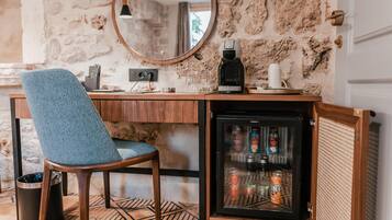 A compact kitchenette with a coffee maker, a refrigerator stocked with beverages, and a chair.