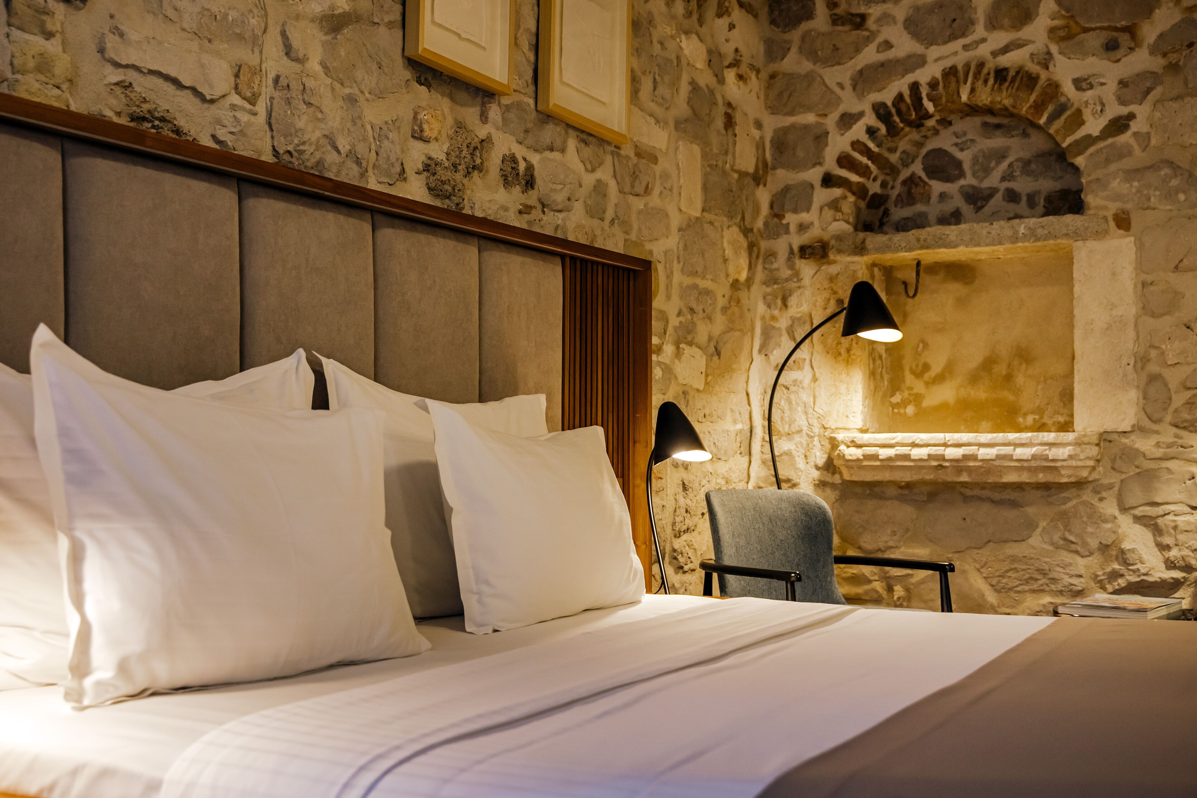A bed with white linens, a headboard, and a stone wall with a fireplace.
