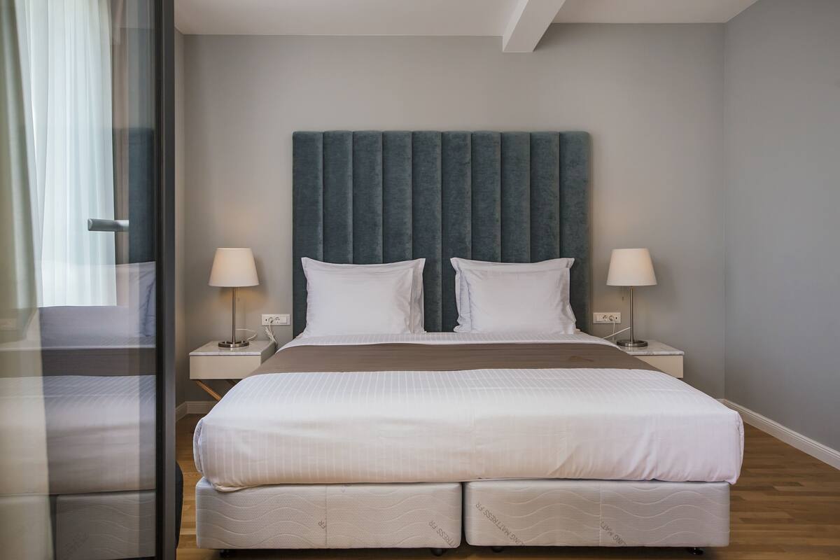 Une chambre d’hôtel moderne avec un grand lit, deux tables de chevet et une grande fenêtre avec des rideaux.