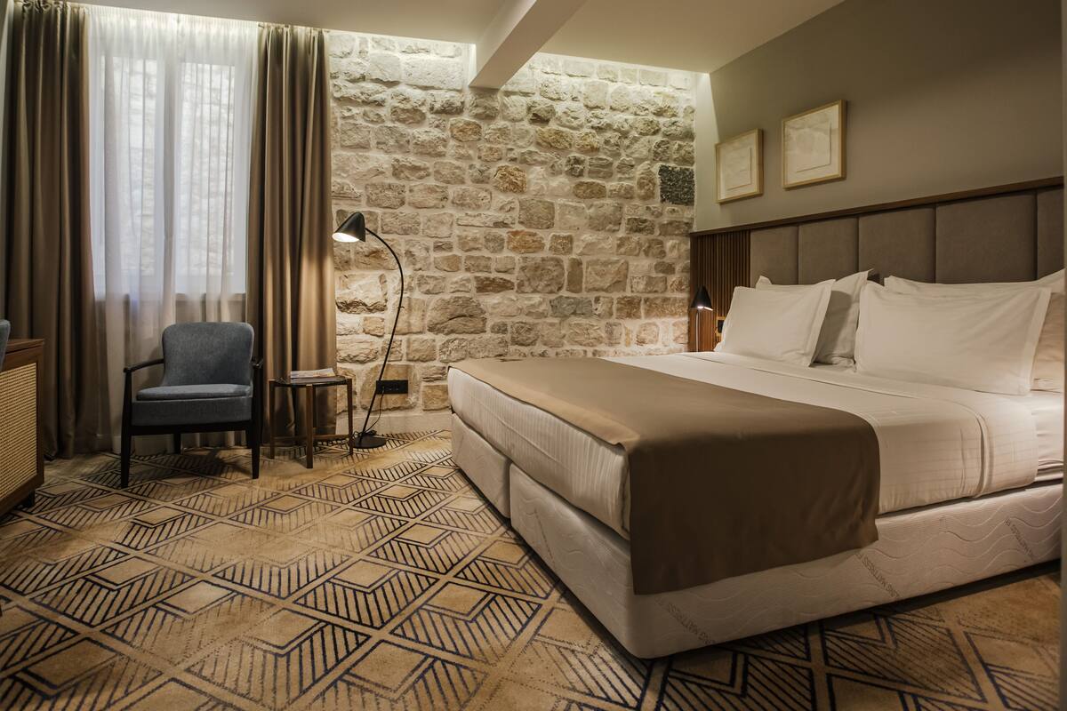 Une chambre d’hôtel avec un grand lit, une chaise, une lampe et un mur en pierre.