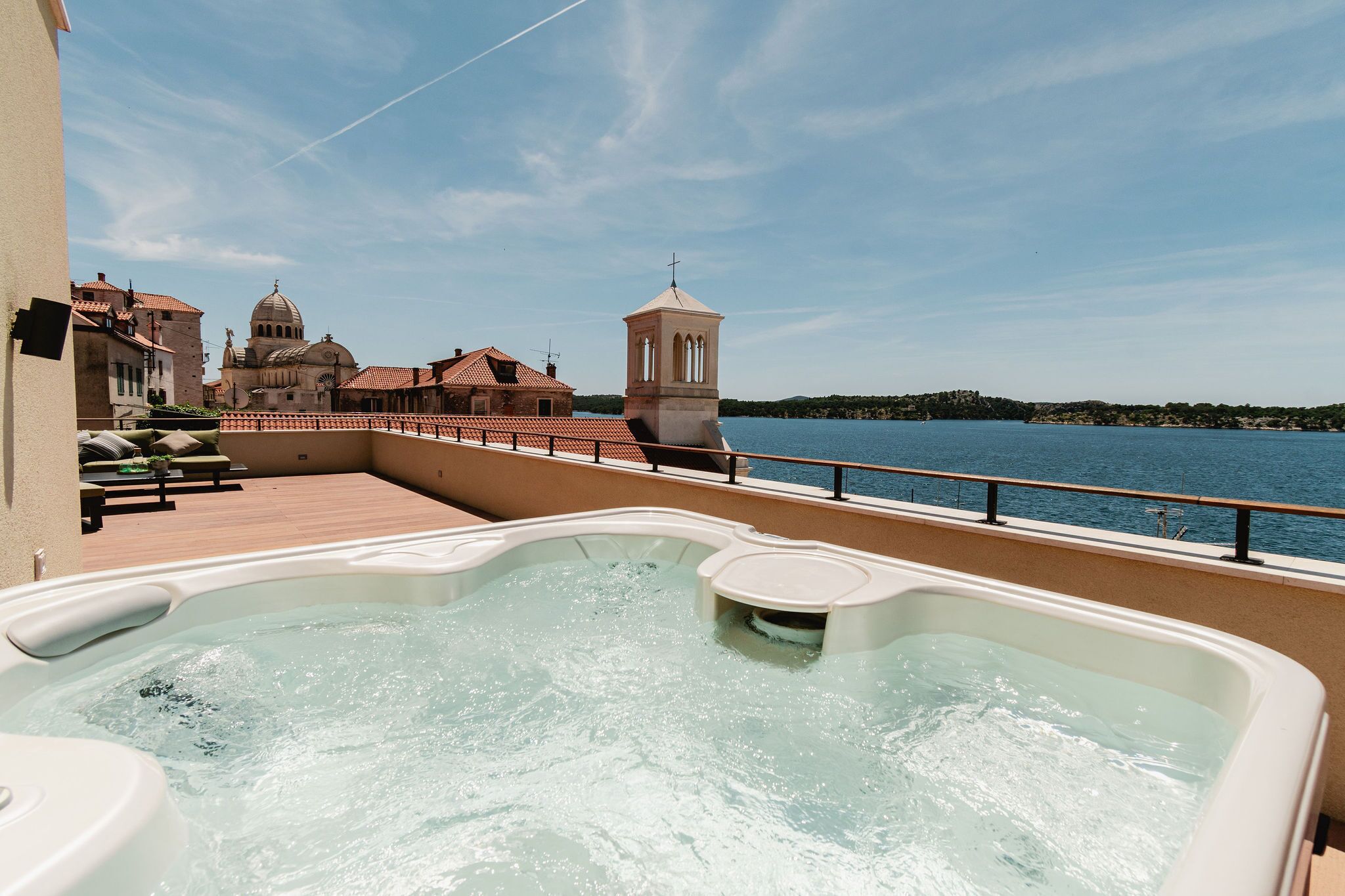 A hot tub on a balcony overlooking a body of water with a church and tower in the background.