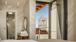 A bedroom with a large bed, a bathroom with a marble wall, and a view of a church tower through a glass door. - Armerun Heritage Hotel (Sibenik)