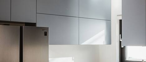 A modern kitchen with grey cabinets, a stainless steel refrigerator, and a marble countertop with a fruit basket.