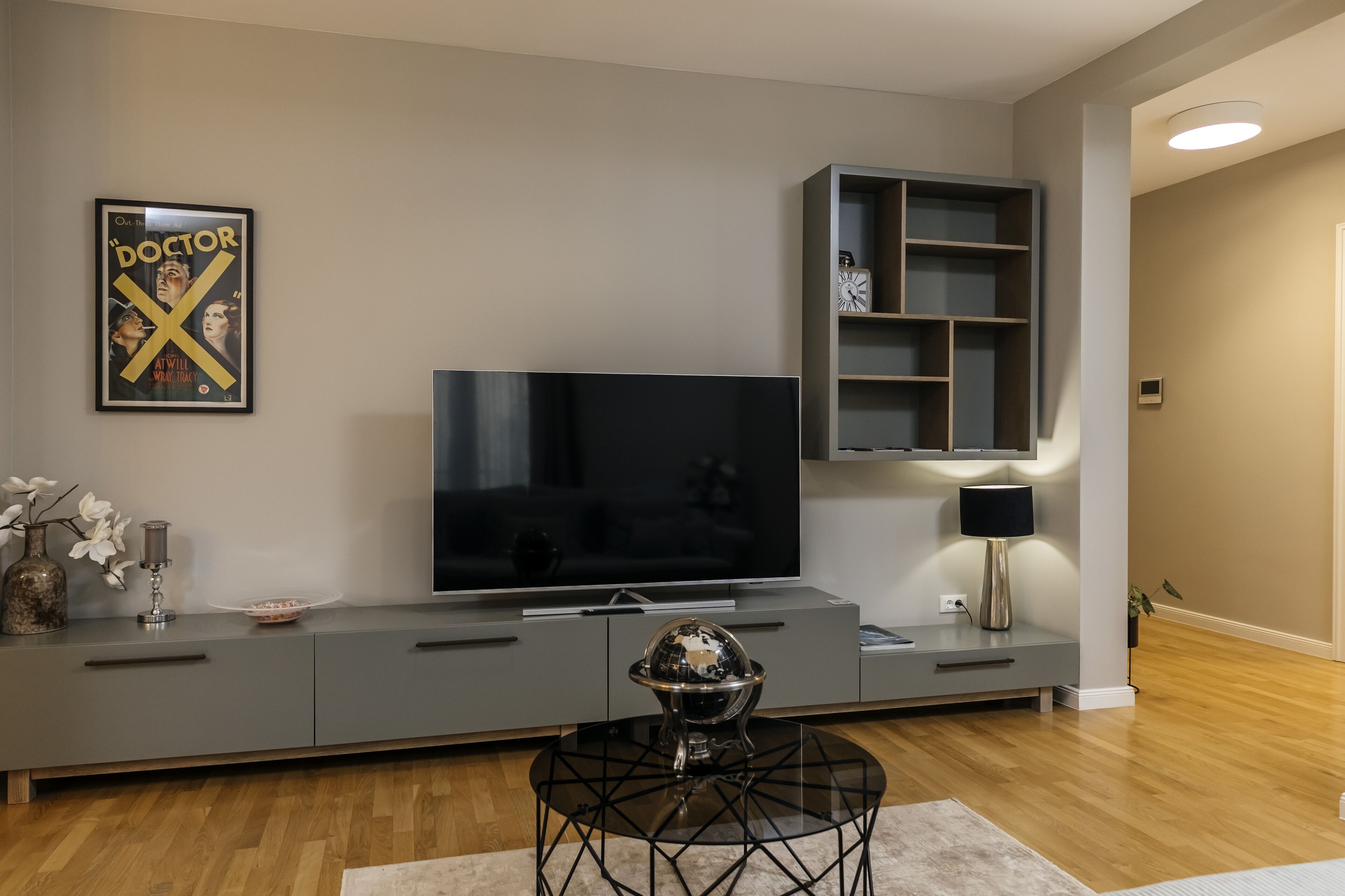 En moderne stue med et fladskærms-tv, en grå multimediemøbel og en dekorativ globus på et glastilbordsbord.