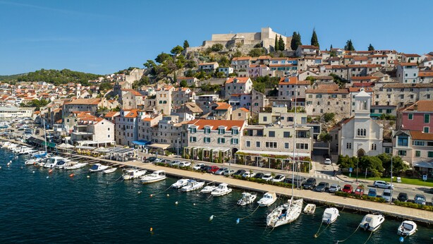 A coastal town with historic stone buildings, a marina with boats, and a prominent castle on a hill. - Armerun Heritage Hotel (Sibenik)