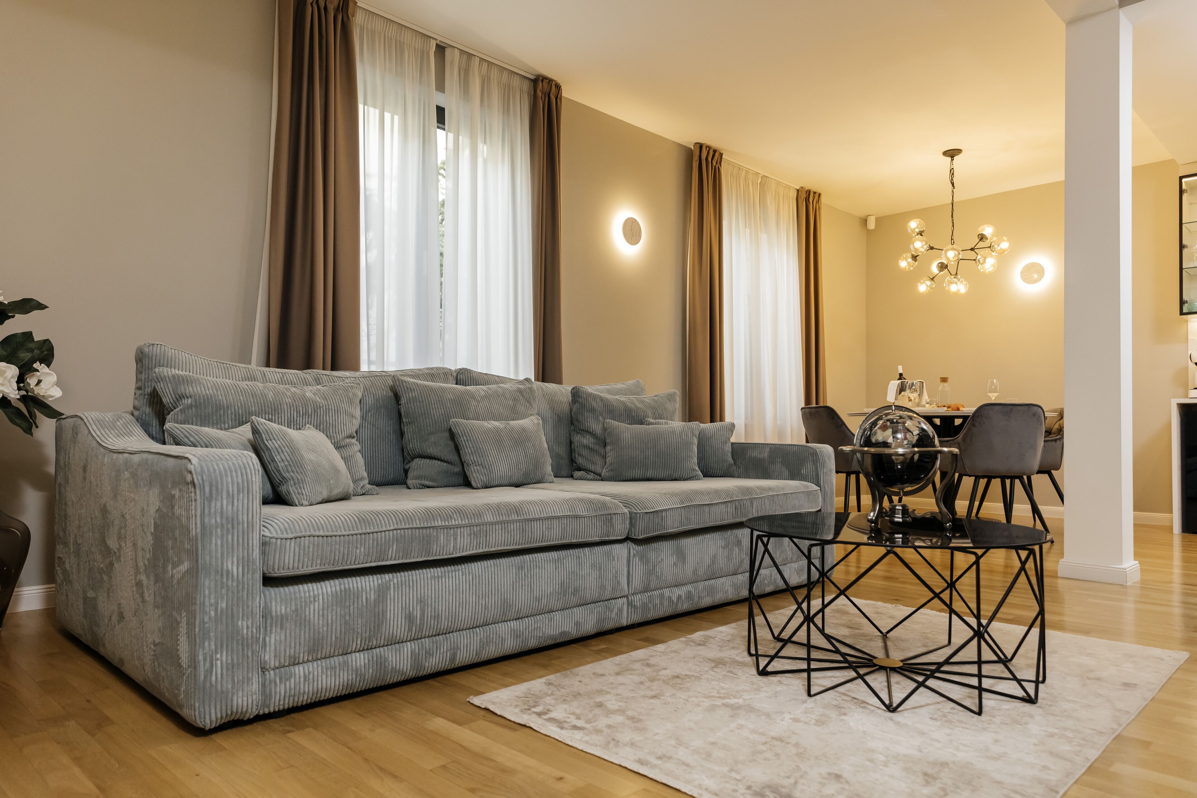 A modern living room with a grey sofa, a coffee table, and a dining area with a chandelier.