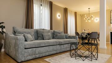 A modern living room with a grey sofa, a coffee table, and a dining area with a chandelier.