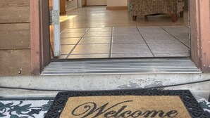 Fachada de madeira com porta de metal, escada com guarda-corrimão azul-turquesa, sofá estampado e um tapete de boas-vindas.