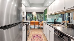 A modern kitchen with stainless steel appliances, a dining area with a rug, and a view of greenery outside. - Spacious Family or Couples Condo - Walk to Coligny Beach & Shops (Hilton Head Island)