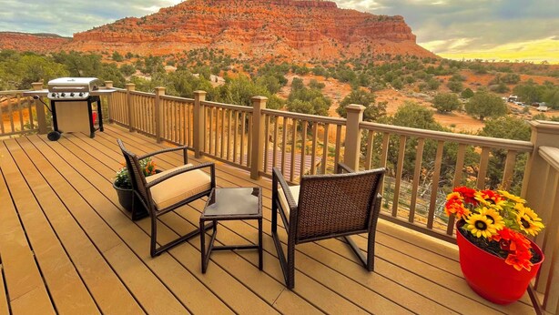 Une terrasse avec un barbecue, des chaises et un pot de fleurs contenant des tournesols.