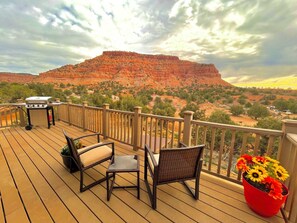 A deck with a grill, chairs, and a potted plant with sunflowers. - Rustic Barn Loft | Kanab Red Cliffs | Pet Friendly (Kanab)