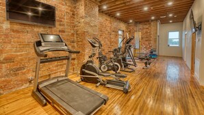 Une salle de sport équipée de divers appareils d’exercice, avec un mur en briques et un plancher en bois.