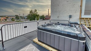 Un jacuzzi sur un balcon offrant une vue sur la ville, avec un mur en briques et une rambarde en bois.