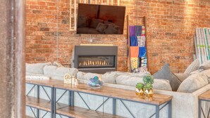 Un salon chaleureux avec des poutres apparentes, un mur en briques, une cheminée et un coin salon confortable.