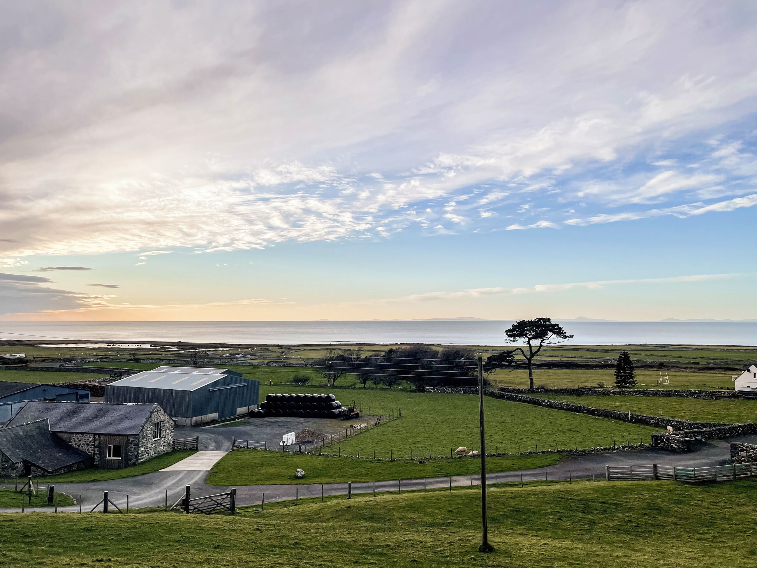 A rural landscape with a large building, possibly a farm or industrial facility, surrounded by green fields and a body of water in the distance.