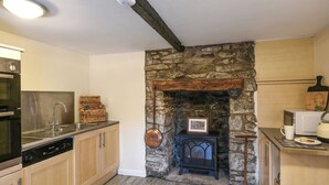 Eine Küche mit Holzausstattung, einem Kamin aus Stein, einer Mikrowelle und einem Spülbecken.