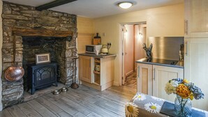 Eine gemütliche Küche mit Kamin aus Stein, Holzbalken, einer Mikrowelle und einem Edelstahl-Kühlschrank.