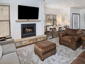 A modern living room with a fireplace, a flat-screen TV mounted above it, and a dining area with a table and chairs. - Canyon Run (Avon)