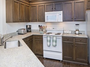 A kitchen with wooden cabinets, a microwave, a stove, a sink, and a coffee maker. - Canyon Run (Avon)