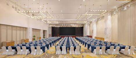 Un salón de conferencias con filas de mesas y sillas, un escenario y una alfombra con diseño de mármol.