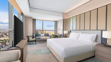 A hotel room with a large bed, a TV, a sofa, a desk, and a view of the city.