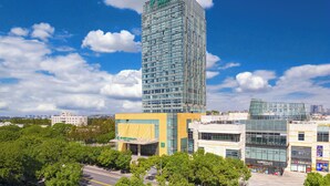 A tall glass skyscraper with a modern design, surrounded by other buildings and trees. - Holiday Inn Shanghai Minhang Center by IHG (Shanghai)