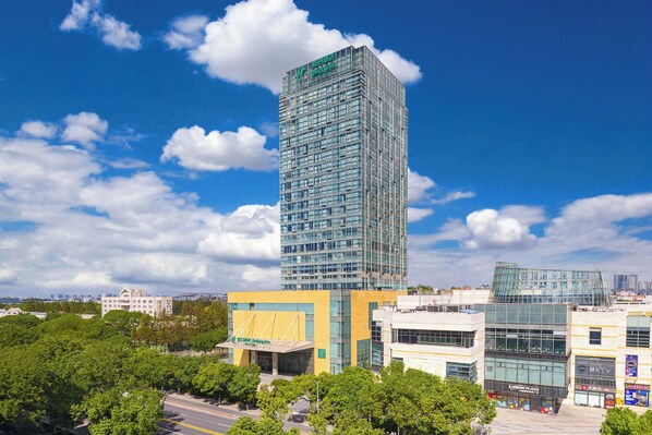 A tall glass skyscraper with a modern design, surrounded by other buildings and trees. - Holiday Inn Shanghai Minhang Center by IHG (Shanghai)
