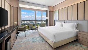 A modern hotel room with a large bed, a flat-screen TV, a desk, and a chair. The room has large windows offering a city view. - Holiday Inn Shanghai Minhang Center by IHG (Shanghai)