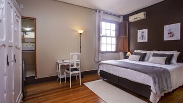 Een slaapkamer met een bed, een bureau, een stoel, een raam met gordijnen en een airconditioning.