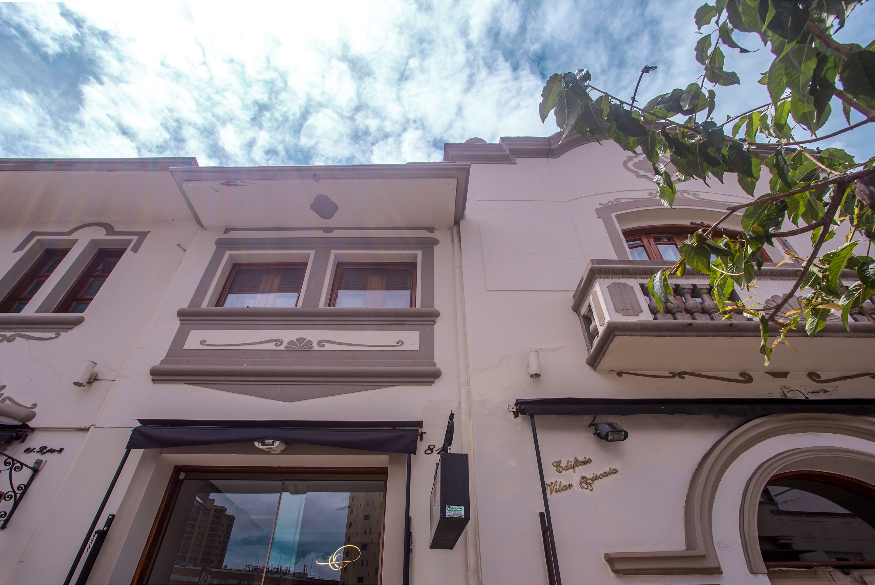 A building with a classic architectural style, featuring a balcony with a railing, a large arched window, and a sign above the entrance.