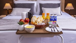 A neatly arranged breakfast tray on a bed with a headboard, including fruits, bread, beverages, and utensils. - Hotel Gambrinus (Poços de Caldas)