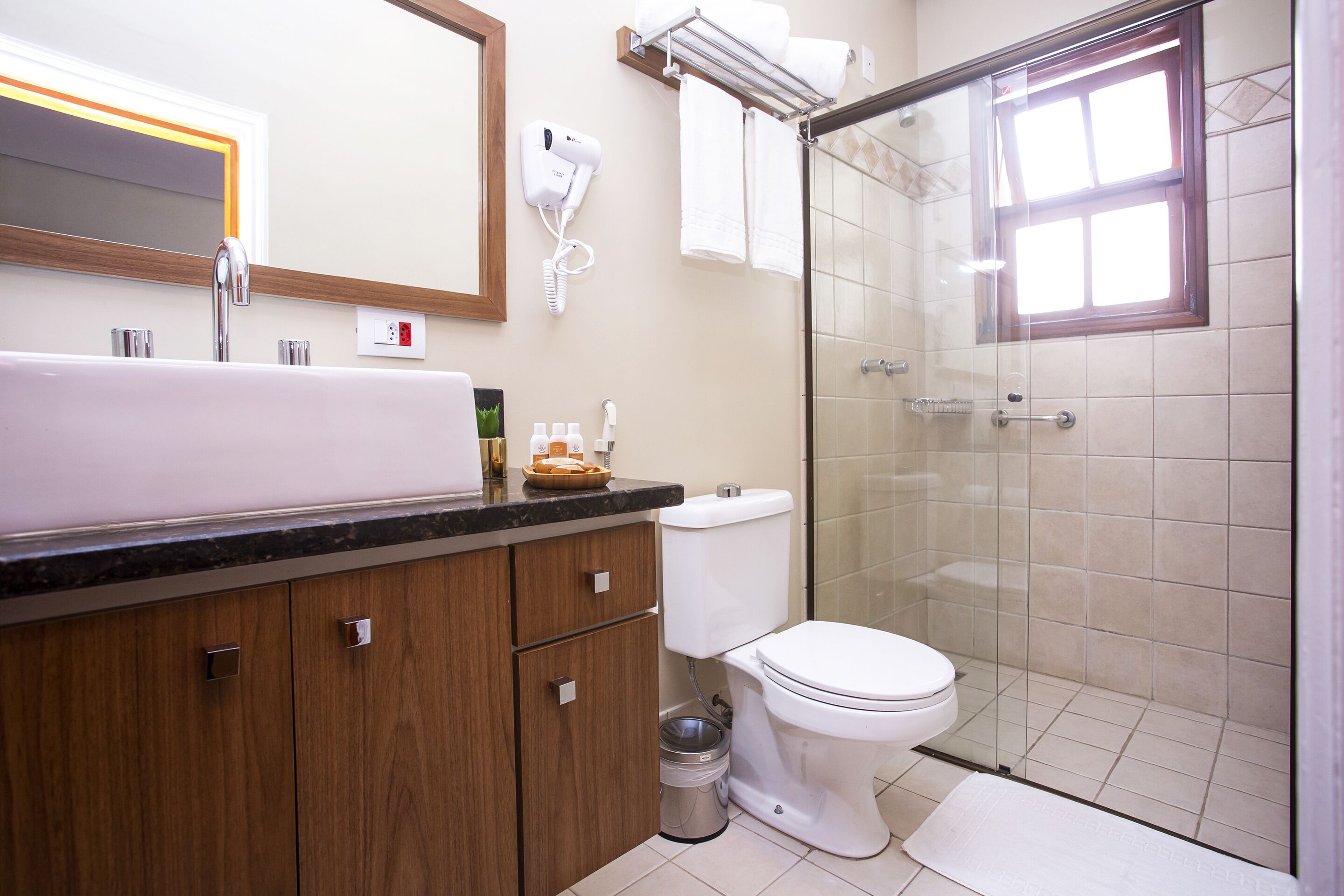 Een moderne badkamer met een groot wastafel, toilet, een douche met glazen wanden en een haardroger bevestigd aan de muur.