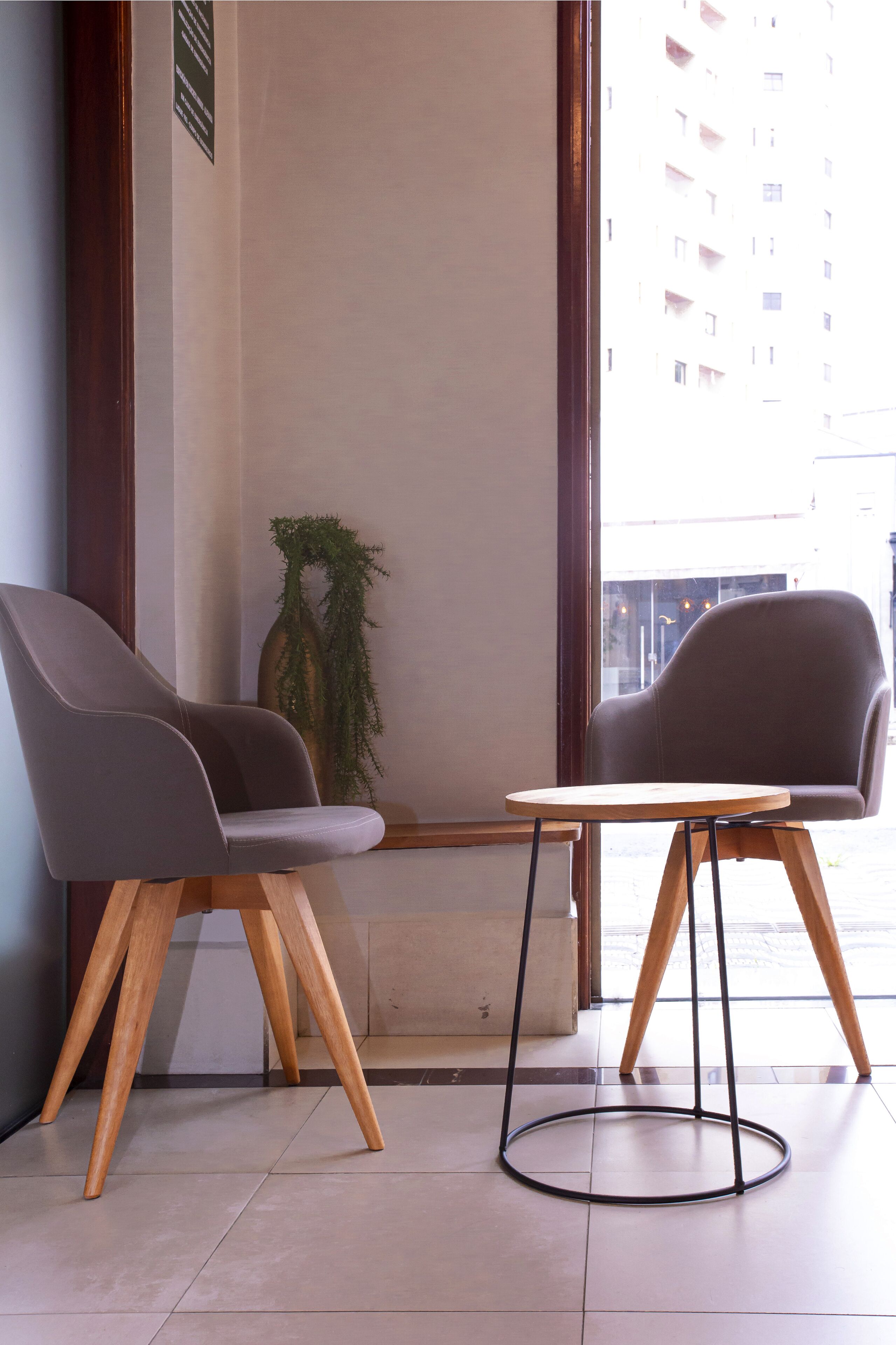 Esquina de una habitación con dos sillas grises y una pequeña mesa de madera con base de metal.
