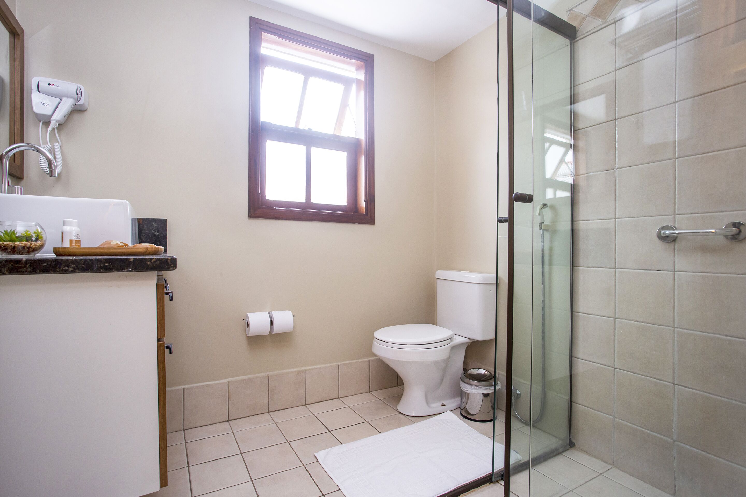 Une salle de bain équipée de toilettes, d’une douche, d’une fenêtre et d’un sèche-cheveux fixé au mur.