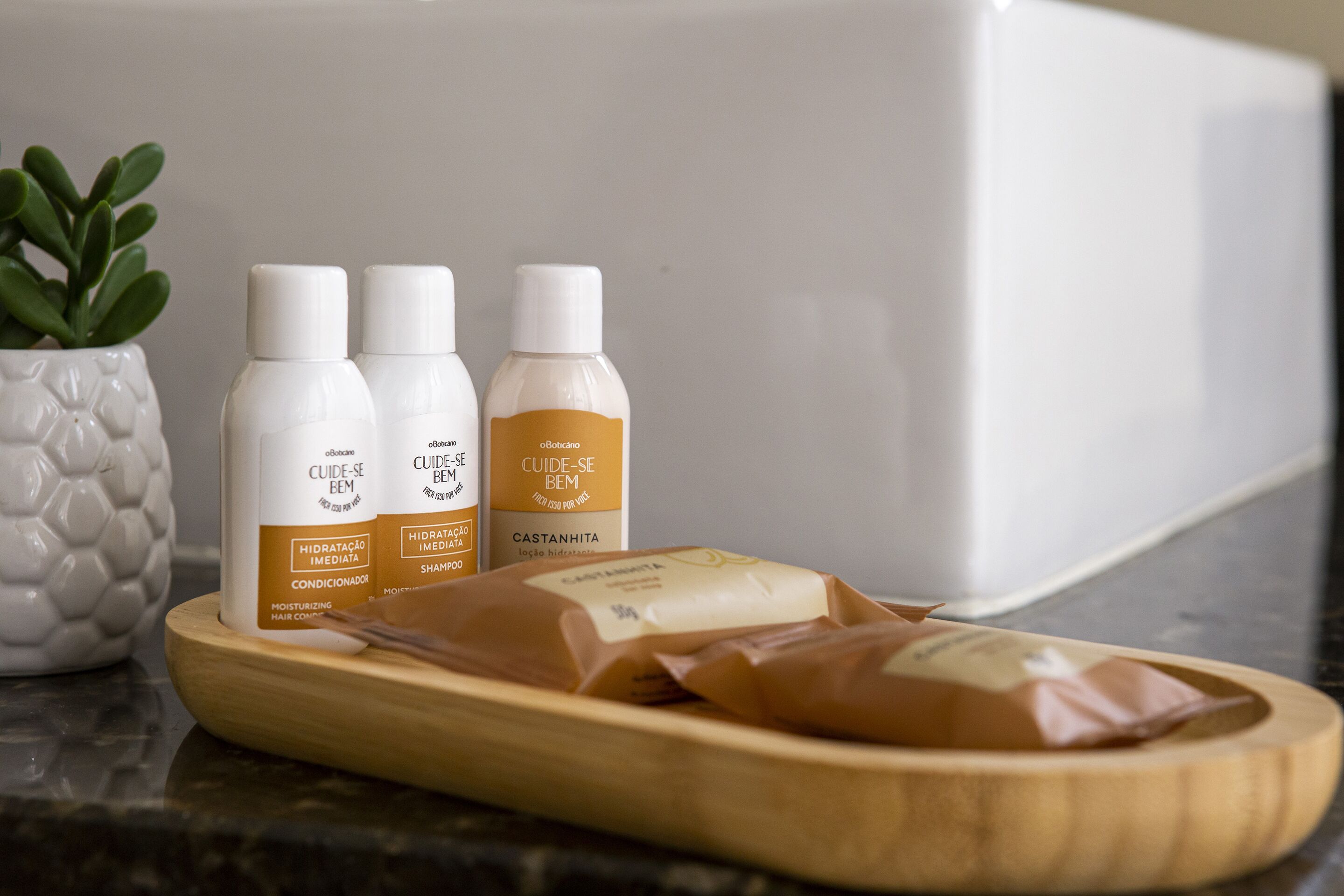 A wooden tray with three bottles of hair care products and a potted plant on a kitchen counter.