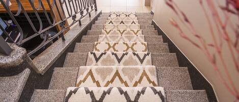 Una escalera con alfombra estampada y peldaños de piedra que conducen a una habitación con una cama y un escritorio.