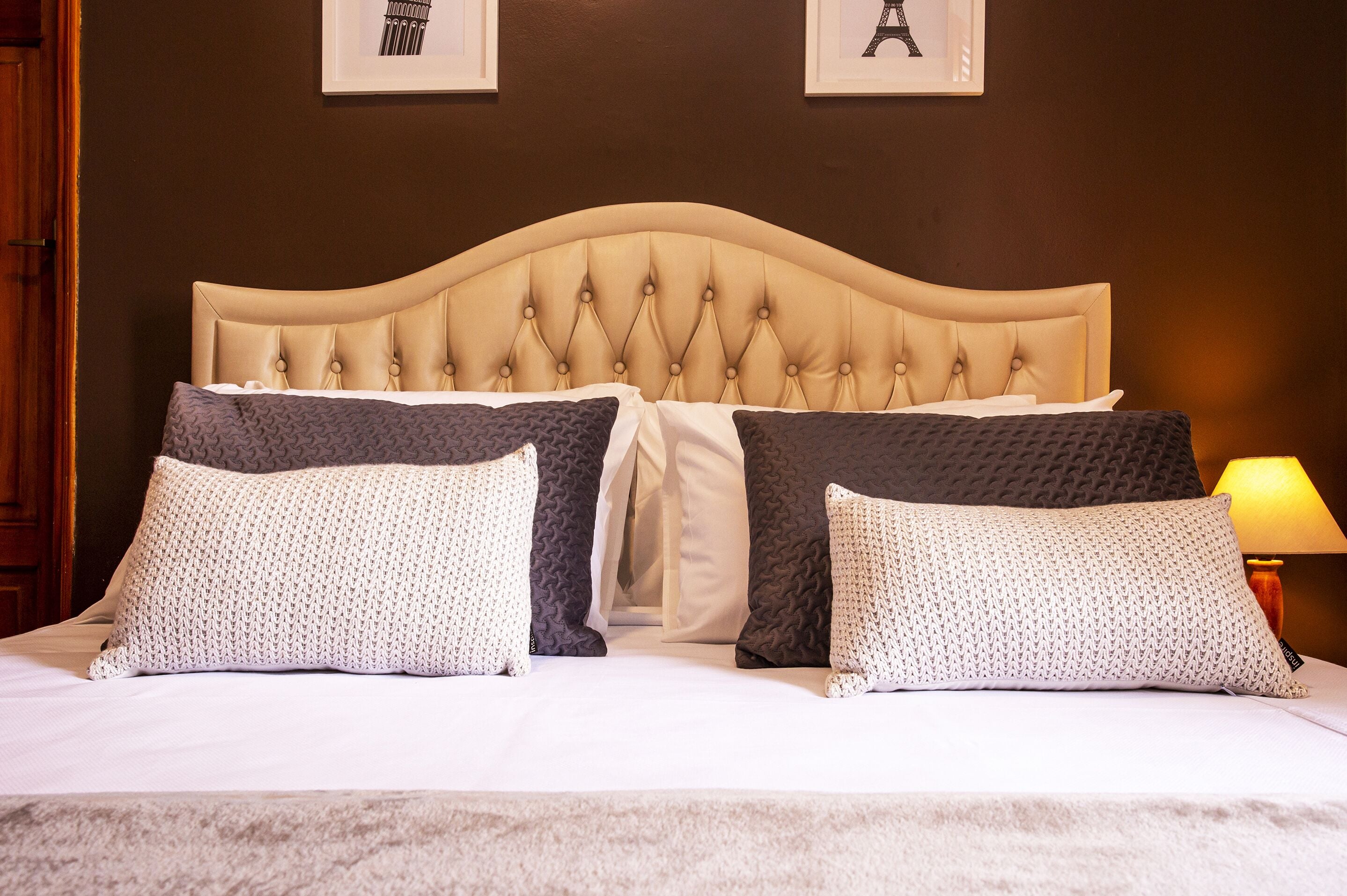 A bed with a tufted headboard, multiple pillows, and a lamp on the side.