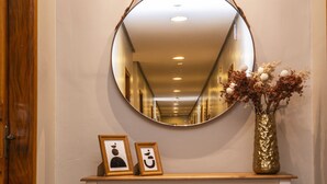 A hallway with a round mirror on the wall, a wooden door, and a shelf with a vase and framed pictures. - Hotel Gambrinus (Poços de Caldas)