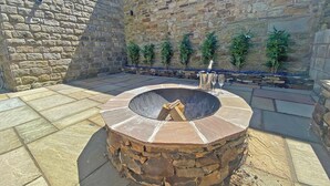 Un muro de piedra, un hoyo para fuego circular de piedra y plantas en macetas.