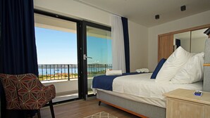 Een hotelkamer met een bed, een stoel, een nachtkastje en uitzicht op zee vanaf een balkon.