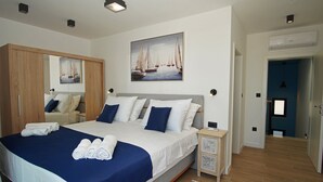 Een moderne slaapkamer met een groot bed, een kledingkast, een schilderij van zeilboten en een badkamer die door een open deur zichtbaar is.