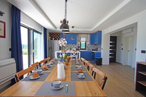 A modern kitchen with blue cabinets, a dining area with a wooden table set for breakfast, and a large window with curtains.