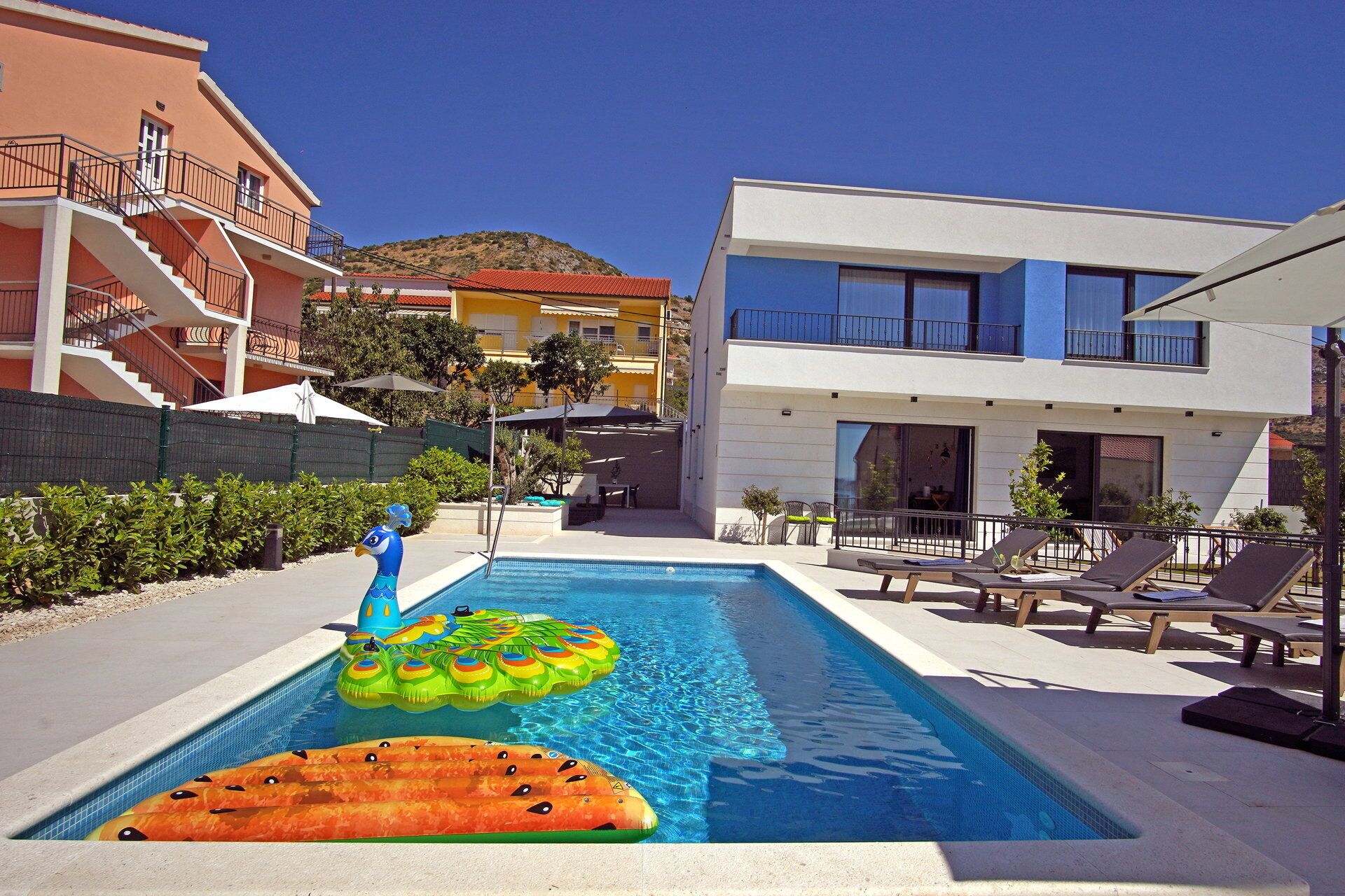 A swimming pool with inflatable toys, lounge chairs, and a building with balconies.