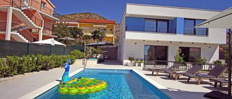 A swimming pool with inflatable toys, lounge chairs, and a building with balconies.
