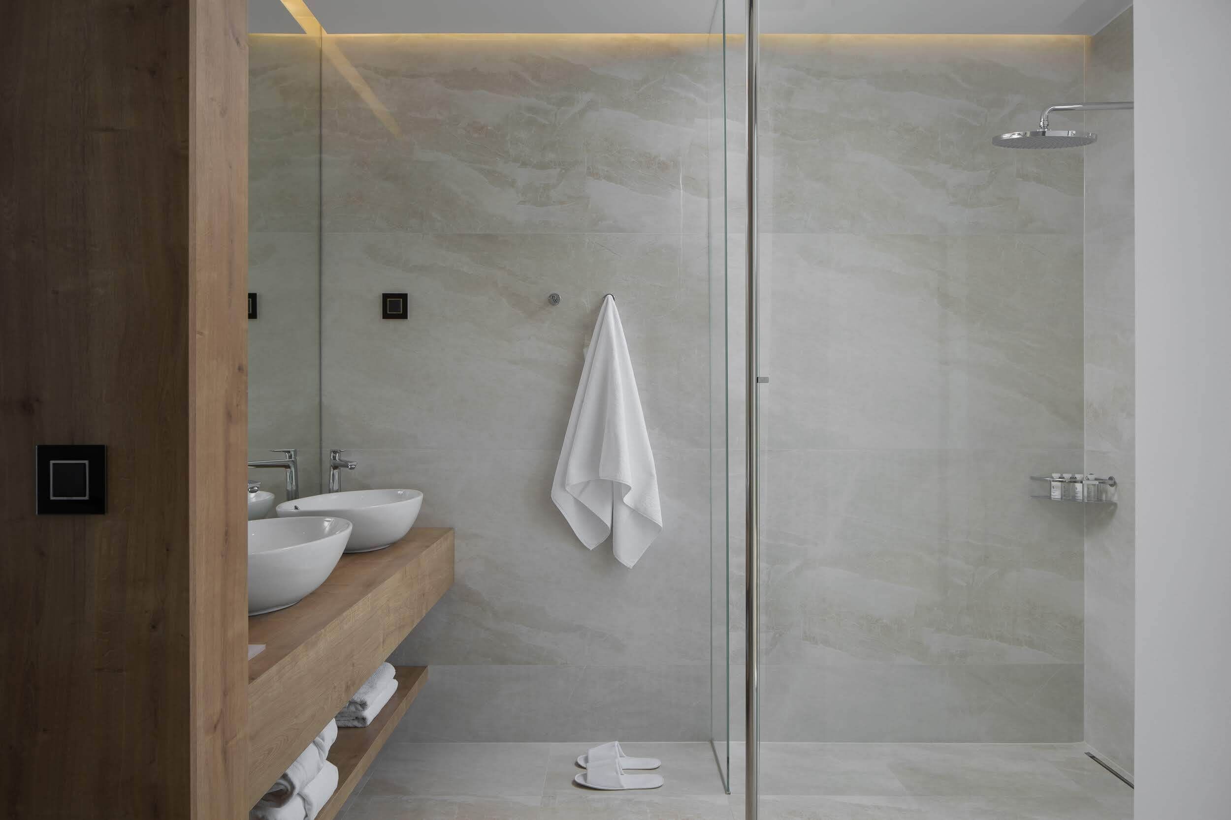 A modern bathroom with a glass-enclosed shower, two sinks, and a wooden vanity.