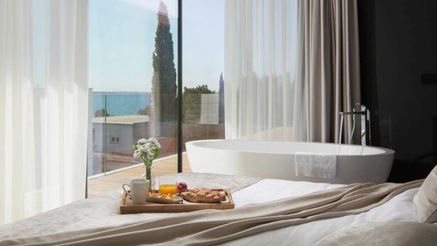 Ein Schlafzimmer mit großem Fenster, einer Badewanne und einem Frühstücksbrett mit Gebäck und Saft.