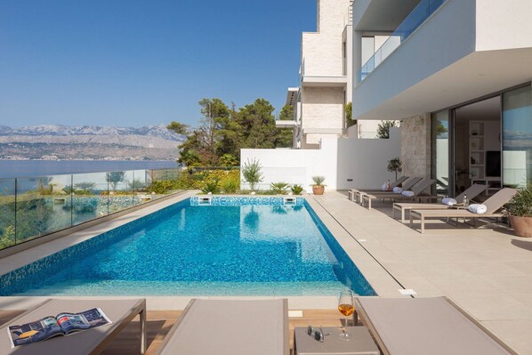 Un área de piscina moderna al aire libre, con vista despejada al mar y montañas al fondo.