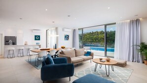 A modern living room with a sofa, chairs, a dining table, and a view of a pool and greenery. - Beachfront Villa Charisma with Pool (Splitska)