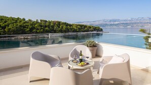 A balcony with a table set for two, overlooking a body of water and a mountainous landscape. - Beachfront Villa Charisma with Pool (Splitska)